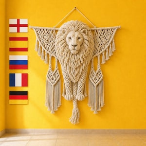 May include: A cream-colored macrame wall hanging featuring a detailed lion head with a full mane, intricate knotted patterns, and long fringe tassels. To the left, five rectangular flags are displayed vertically in a column on the yellow wall.