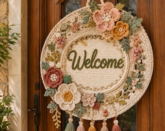 May include: A circular crochet wall hanging featuring a cream-colored base with the word Welcome embroidered in green. The piece is decorated with various crocheted flowers in shades of pink, orange, and white, green leaves, and five hanging tassels.