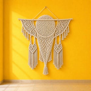 May include: A large off-white macrame wall hanging featuring a central circular woven section, intricate knotted patterns, and multiple hanging fringe tassels suspended from a horizontal wooden dowel with a triangular cord for wall mounting.
