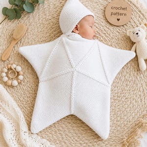 Könnte beinhalten: Eine weiße gestrickte Baby-Wickeldecke in Form eines fünfzackigen Sterns mit passender spitzer Mütze. Die Wickeldecke weist ein strukturiertes Strickmuster auf und wird mit einer Holzscheibe mit der Aufschrift crochet pattern präsentiert.