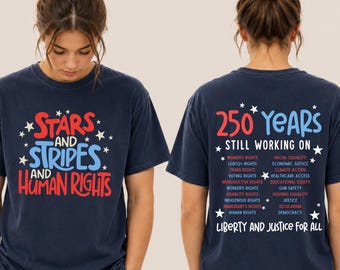 Könnte beinhalten: Ein marineblaues T-Shirt mit rotem und hellblauem Text auf der Vorderseite, der Stars and Stripes and Human Rights mit weißen Sternen lautet. Die Rückseite zeigt 250 Years Still Working On mit einer Liste von Rechten und Liberty and Justice For All.