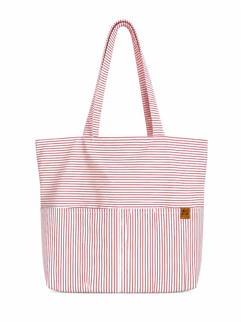 May include: A tote bag featuring a red and white horizontal striped pattern on the upper section and a red and white vertical striped pattern on the lower section. It includes two shoulder straps and a small brown rectangular label with text.