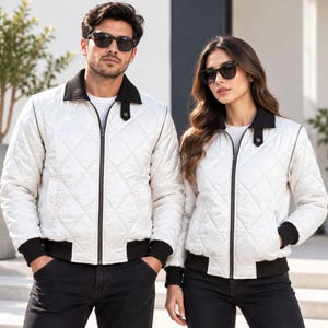 May include: A white quilted bomber jacket featuring a black collar, black ribbed cuffs, and a black ribbed hem. The jacket has a full-length front zipper closure, a diamond-stitched pattern across the body, and two side pockets.