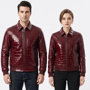 Puede incluir: Dos chaquetas color burdeos a juego con una textura brillante de piel de cocodrilo, que presentan un cuello clásico, una cremallera frontal completa y puños y dobladillo acanalados. Las chaquetas tienen un corte estructurado y acabado brillante.