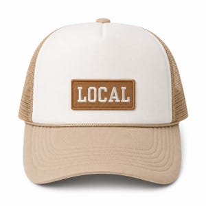 Può includere: Un cappellino trucker con pannello frontale bianco, visiera color sabbia e pannelli posteriori in rete dello stesso colore. Una toppa rettangolare marrone è centrata sul davanti con la parola LOCAL ricamata in lettere maiuscole bianche. Un cordino decora la base.