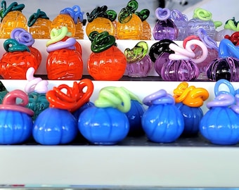 Può includere: Una collezione di zucche decorative in vetro colorato, in varie dimensioni e tonalità, tra cui arancione, blu, verde e viola. Ogni zucca presenta un gambo o una parte superiore in vetro unico e a spirale, creando un'esposizione stravagante.