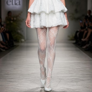 May include: A white tiered mini skirt with a textured surface paired with white lace patterned tights and white pointed-toe pumps with ankle straps. The ensemble features a consistent white color palette and intricate floral lace detailing on the hosiery.