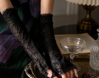 May include: A pair of black sheer fingerless gloves featuring a delicate spiderweb pattern throughout the fabric. The gloves extend to the mid-forearm and are finished with a subtle ruffled trim at the top and bottom edges of the garment.
