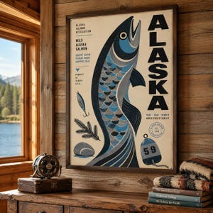 May include: A framed poster featuring a stylised blue and grey salmon, the word ALASKA in large black letters, a fishing lure, a pine branch, a stone, and a blue buoy with the number 59. Text includes Alaska Salmon Association and product details.