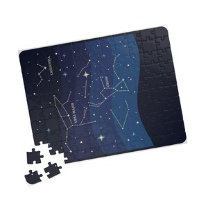 Puede incluir: Un rompecabezas rectangular con un fondo de cielo nocturno azul oscuro y constelaciones de estrellas blancas. El rompecabezas muestra los nombres Cassiopeia, Ursa Major y Orion en texto blanco. Tres piezas sueltas están situadas abajo a la izquierda.