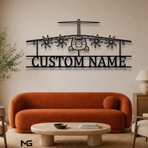 Puede incluir: Una pieza de arte mural de metal negro que presenta la silueta detallada de un avión de transporte militar de cuatro motores. Debajo del avión, el texto CUSTOM NAME se muestra en letras mayúsculas negritas, integrado en el diseño del marco.