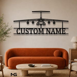 May include: A black metal wall art piece featuring a silhouette of a cargo airplane with four engines and a T-tail design. Below the aircraft, the text CUSTOM NAME is displayed in a bold, capitalized font, integrated into the linear structure.