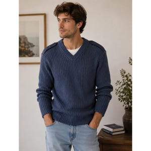 Puede incluir: Un suéter azul con cuello en V, textura de punto acanalado y charreteras en los hombros. La prenda de manga larga se lleva sobre una camiseta blanca y se combina con pantalones vaqueros azul claro, creando un estilo superpuesto con cuello.