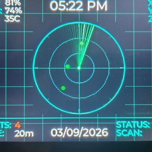 May include: A digital radar display screen with a black background and bright cyan grid lines. The interface shows text including Armor: 81%, Ammo: 74%, Temp: 35C, Targets: 4, Range: 20m, Status: Green, and Scan: Active, with a central circular radar sweep.