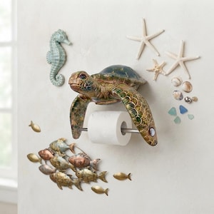 May include: A wall-mounted sea turtle toilet paper holder with a metallic green and brown finish. The turtle holds a silver rod with a roll of white toilet paper. Decorative wall accents include a seahorse, starfish, seashells, and fish.