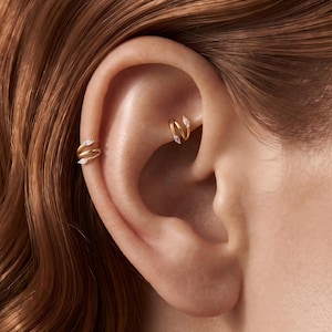 May include: Two gold spiral earrings featuring small marquise-cut clear stones at each end. One earring is positioned on the outer ear cartilage, while the other is placed in the rook area of the ear, both showcasing a polished metallic finish.