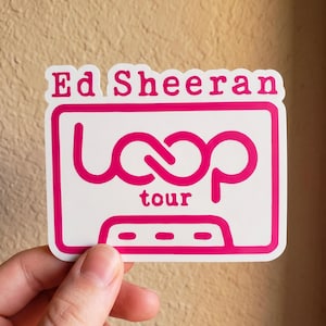 May include: A white rectangular sticker with rounded corners featuring the hot pink text Ed Sheeran at the top. Below, a hot pink outline of a cassette tape contains the stylized hot pink text loop tour in the center and three small rectangles.