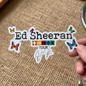 May include: A die-cut sticker featuring the text Ed Sheeran in black, with colorful mathematical symbols, the word TOUR, and a black signature below. The design is decorated with five butterflies in yellow, red, orange, green, and blue colors.