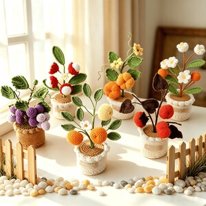 Op de afbeelding: Een verzameling van zes kleine potplanten gemaakt van haakgaren. Elke plant heeft groene bladeren en diverse vruchten of bloemen, waaronder paarse druiven, rode lychees, oranje pompoenen, gele citrusvruchten en witte bloemen in textuurrijke potten.