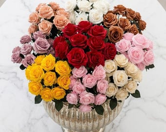 May include: A large, multi-colored bouquet of artificial roses in shades of red, white, yellow, pink, mauve, and brown, arranged in a metallic, ribbed, pedestal-style vase. The roses feature layered petals and green stems.