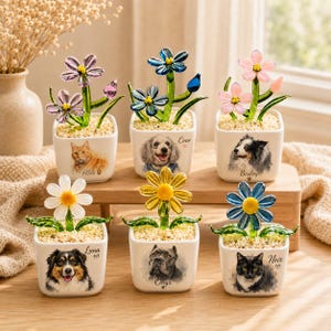 Puede incluir: Seis macetas cuadradas de cerámica blanca, cada una con una flor de vidrio con tallos verdes y un retrato de mascota. Las macetas presentan imágenes de un gato, un caniche, un border collie, un pastor australiano, un cane corso y un gato negro.