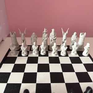 May include: A chess set featuring white molded plastic pieces arranged on a black and white checkered board. The white pieces include detailed character figures, towers, and busts, positioned in two rows at the edge of the game board surface.