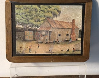 May include: A rectangular framed print depicting a rural scene with a wooden house, a brick chimney, and a large tree. Several figures are present in the yard, along with chickens, a dog, and colorful quilts hanging on a clothesline.