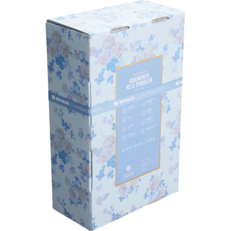 May include: A rectangular cardboard product box featuring a light blue background with a repeating pattern of pink and blue roses. The box displays the text Quencher H2.0 Tumbler, Stanley, and LoveShackFancy, along with various product icons.