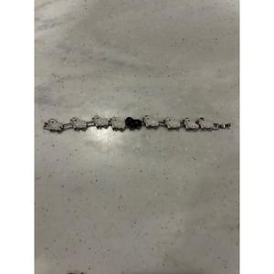 Puede incluir: Una pulsera de eslabones en tono plateado que presenta una serie de pequeños dijes de ovejas. Siete de las ovejas son blancas con detalles negros, mientras que una oveja situada cerca del centro es de color negro sólido y unidas por eslabones.