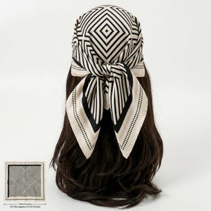 May include: A square headscarf featuring a black and cream geometric diamond pattern with a dotted border. The scarf measures 27.5 x 27.5 inches. It is tied in a knot at the back, displaying a repeating linear design on a smooth fabric surface.