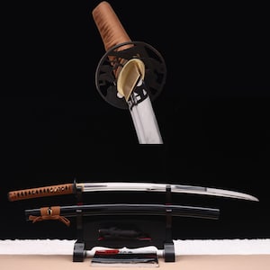 May include: A katana sword with a polished steel blade, a brown wrapped handle, and a black circular tsuba guard. The sword rests horizontally on a black stand alongside its matching black scabbard, which features a brown cord accent.
