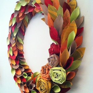 May include: A fall-themed paper wreath with brown, orange, red, and green paper leaves. The wreath is decorated with paper flowers in shades of brown, orange, red, and green.