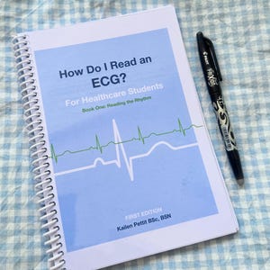May include: A spiral-bound educational book titled How Do I Read an ECG? For Healthcare Students, Book One: Reading the Rhythm by Kailen Pettit BSc, BSN, First Edition, featuring a light blue cover with a green and white heart rhythm graphic and a black pen.