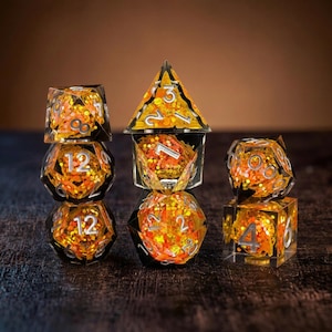 May include: A set of polyhedral dice made of clear resin filled with orange and gold glitter. The dice feature silver-coloured numbers and include various geometric shapes such as a tetrahedron, octahedron, dodecahedron, and icosahedron.
