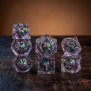Könnte beinhalten: Ein Set aus polyedrischen Würfeln aus klarem Harz, die jeweils einen wirbelnden Kern aus irisierendem violettem, blauem und grünem Glitzer enthalten. Die Würfel haben eingravierte silberfarbene Zahlen, darunter ein W20, W12, W10, W8, W6 und W4.