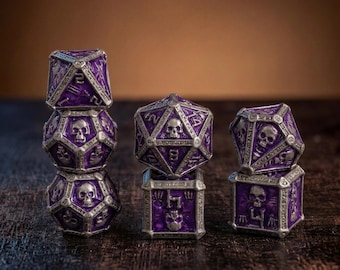 May include: A set of polyhedral dice featuring a deep purple enamel finish with intricate silver-toned metal frames. Each die face displays embossed skull motifs and numerical markings. The collection includes various geometric shapes stacked in three distinct groups.