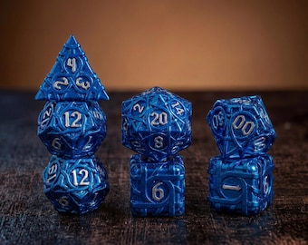 May include: A set of seven polyhedral dice in a metallic blue finish with silver-colored numbers. The dice feature an intricate, raised lattice or vine-like pattern across their surfaces. The set includes various shapes, including a d20, d12, d10, d8, d6, and d4, arranged in three small stacks.