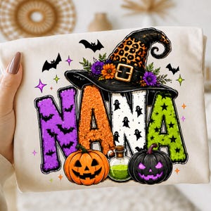 Puede incluir: Una camiseta color crema con un gráfico que deletrea NANA en letras coloridas y estampadas. El diseño incluye un sombrero de bruja con estampado de leopardo, flores moradas y naranjas, murciélagos, fantasmas, dos calabazas y una poción.