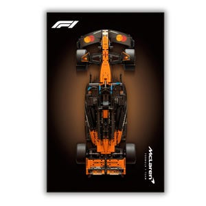 May include: A top-down view of a McLaren Formula 1 team race car model in orange and black. The F1 logo is in the top left corner, and the McLaren Formula 1 team text is in the bottom right. The car features detailed mechanical components.