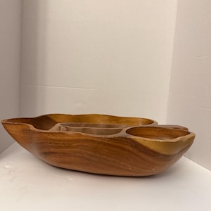 Könnte beinhalten: Eine große, organisch geformte Servierschale aus Holz mit natürlicher Maserung und einer glatten, polierten Oberfläche. Die Schale verfügt über mehrere integrierte Fächer unterschiedlicher Größe, die direkt aus dem Holz geschnitzt sind.