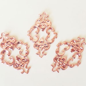May include: Three rose gold metal decorative embellishments with a floral design.