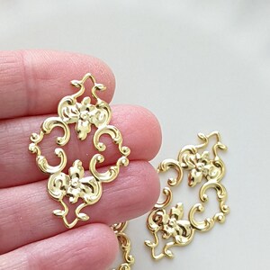 May include: Gold metal decorative embellishments with a floral design. The embellishments are intricate and detailed, with a delicate scrollwork pattern.