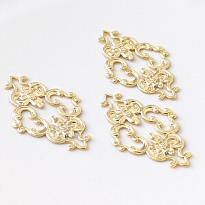May include: Three gold-colored metal decorative embellishments with a floral design. Each embellishment is shaped like a diamond and has intricate details.