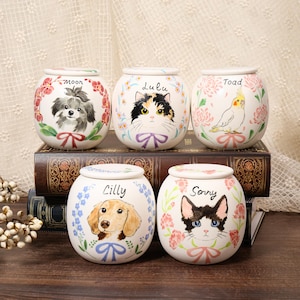 May include: Five round white ceramic jars with lids, each featuring a hand-painted portrait of a pet and a floral wreath. The jars are labeled with the names Moon, Lulu, Toad, Lilly, and Sorry, and each includes a painted ribbon detail below the pet.