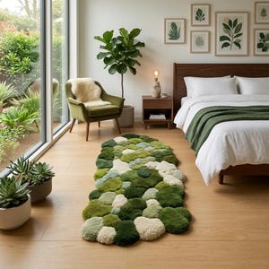 May include: An irregular, organic-shaped area rug featuring a textured, tufted surface composed of various shades of green and cream, resembling a cluster of mossy stones or pebbles, placed on a light-toned wooden floor in a bedroom setting.