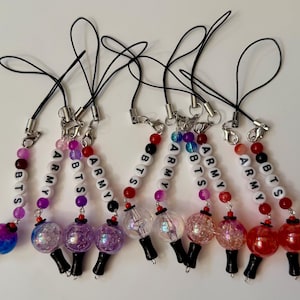 Puede incluir: Un conjunto de nueve colgantes para tel&eacute;fono con cordones negros, cierres de mosquet&oacute;n plateados y cuentas de letras blancas que forman BTS y ARMY. Cada colgante incluye cuentas esf&eacute;ricas coloridas, transl&uacute;cidas y brillantes con bases negras.