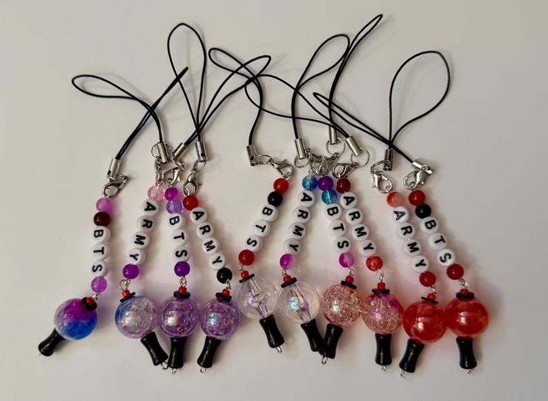 Puede incluir: Un conjunto de nueve colgantes para tel&eacute;fono con cordones negros, cierres de mosquet&oacute;n plateados y cuentas de letras blancas que forman BTS y ARMY. Cada colgante incluye cuentas esf&eacute;ricas coloridas, transl&uacute;cidas y brillantes con bases negras.
