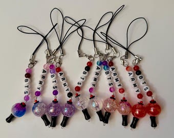 May include: A collection of nine phone charms featuring black cords, silver-tone lobster clasps, and white letter beads spelling BTS and ARMY. Each charm includes colourful, translucent, and glittery spherical beads with black base accents.