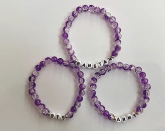 May include: Three circular beaded bracelets made of translucent purple crackle glass beads. Each bracelet features white spherical letter beads spelling out the words BANGTAN, BTS, and ARMY respectively, integrated into the bead strands.
