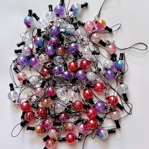 Puede incluir: Una colecci&oacute;n de numerosos dijes esf&eacute;ricos con textura agrietada y acabado iridiscente en tonos rojo, morado, rosa, azul y transparente. Cada dije est&aacute; unido a un lazo de cord&oacute;n negro con un peque&ntilde;o conector de metal de tono plateado.